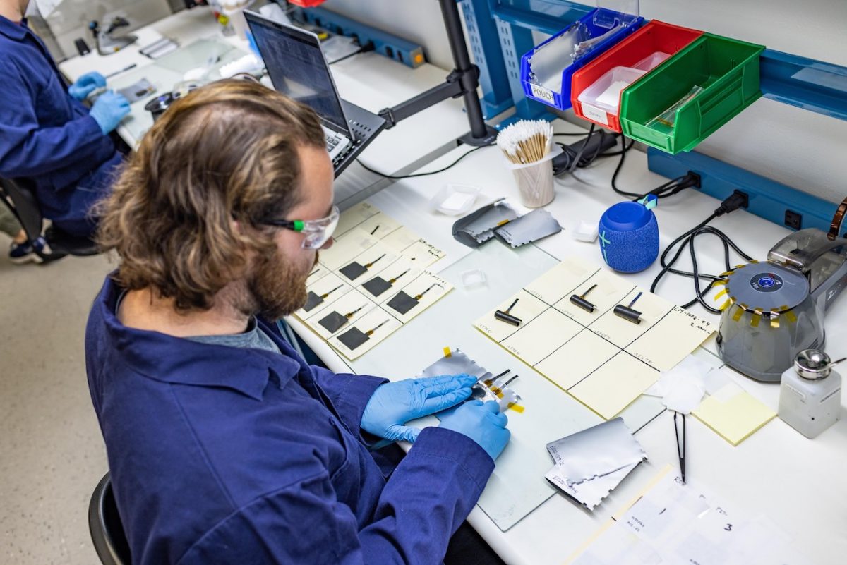 A man wearing blue overalls and blue gloves creating a battery from components